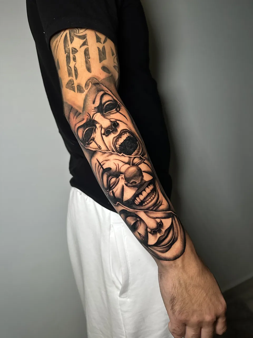 Tatuaje realista en negro y gris de las máscaras de la comedia y la tragedia en el antebrazo, hecho por Guti en Yokai Tattoo Málaga